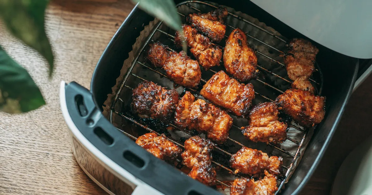 Cestello aperto di una friggitrice ad aria con bocconcini di pollo dorati