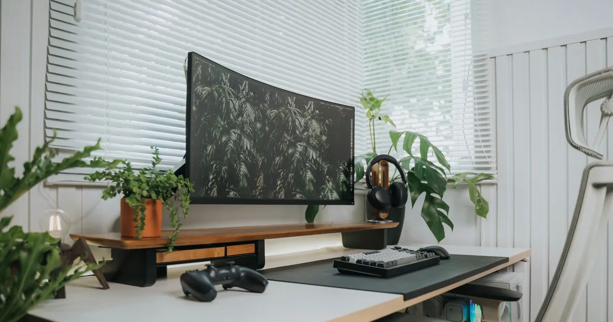 Monitor curvo ultrawide su una scrivania con tastiera, controller e piante